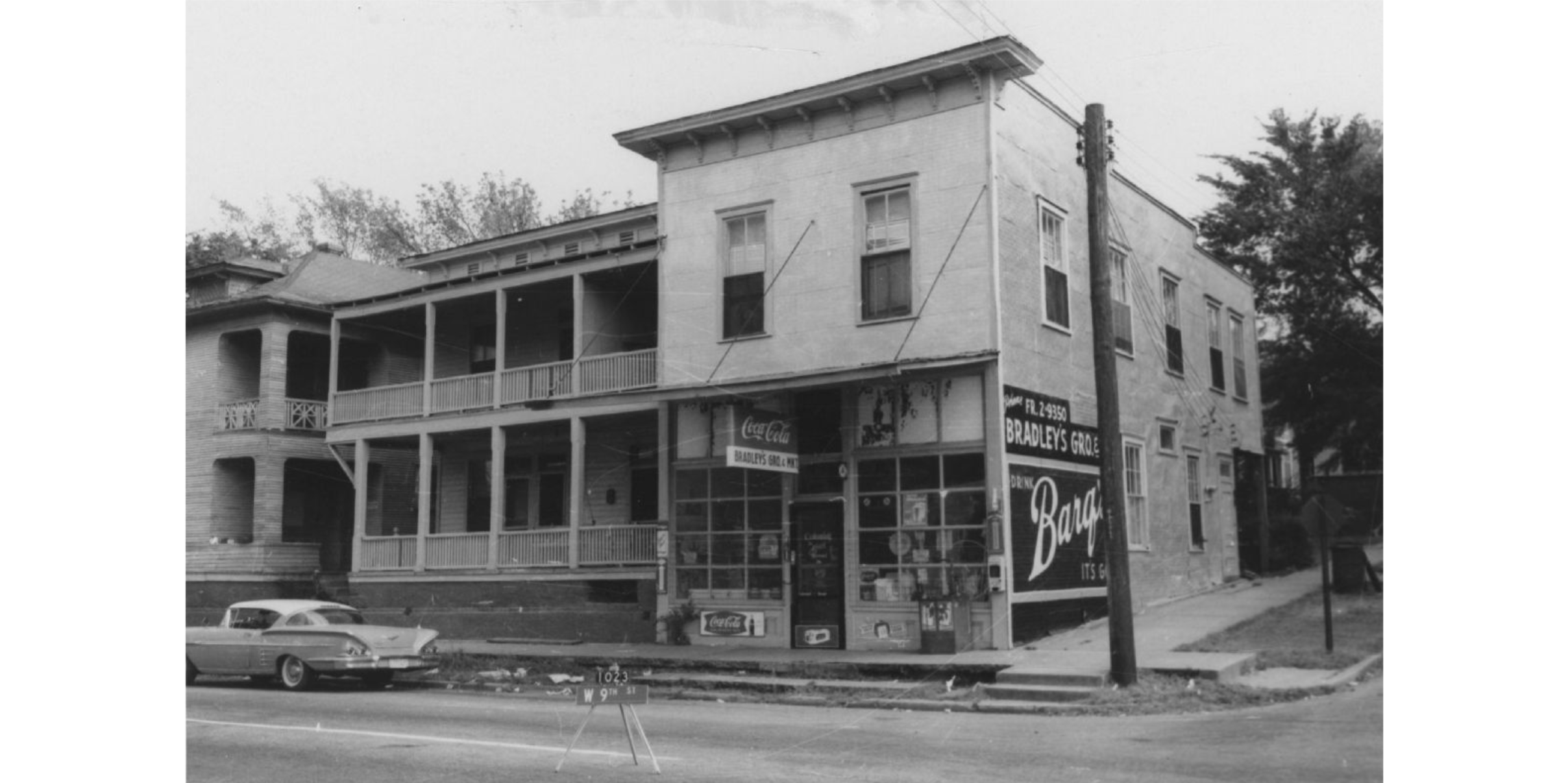 A two-story building on a corner lot. Coca-Cola and Barq's advertisements are on the front and side of the building.