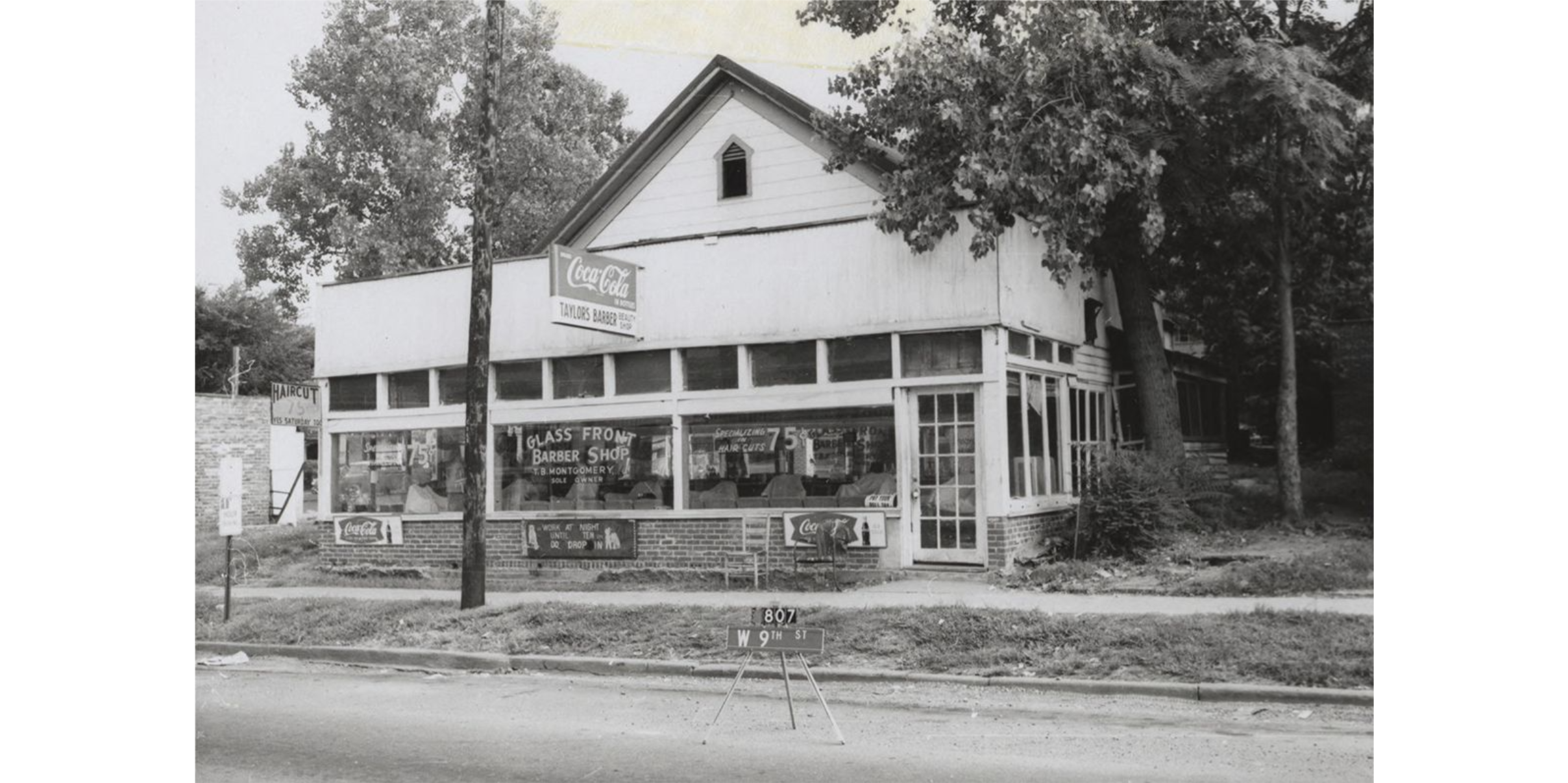 A building with large glass windows across the front. The central window reads: "Glass Front Barber Shop. T.B. Montgomery. Sole Owner." 