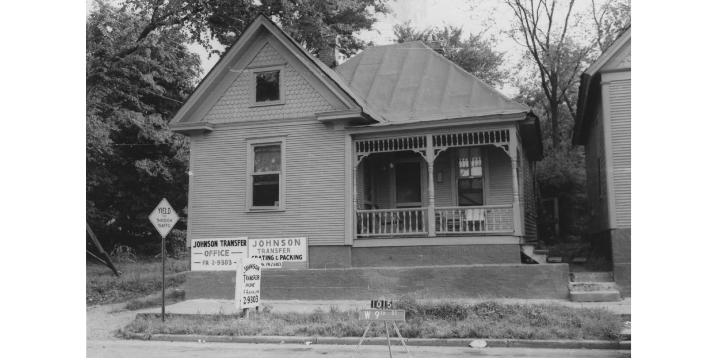 The front of a house with signs for "Johnson Transfer Office" and "Johnson Transfer Crating and Packing" mounted to the bottom left corner of the building.