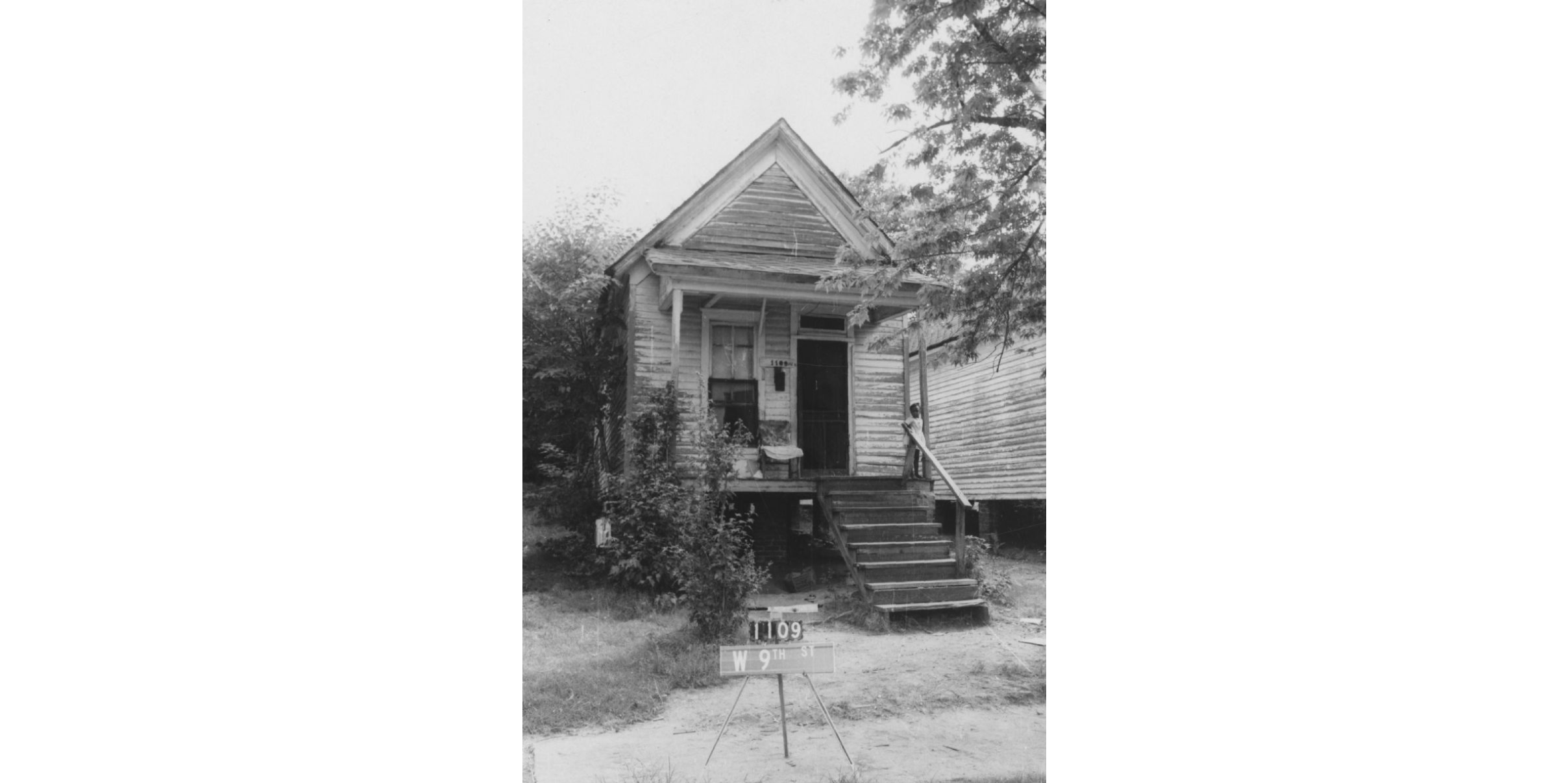 A small, wood-frame house with a child standing on the porch.