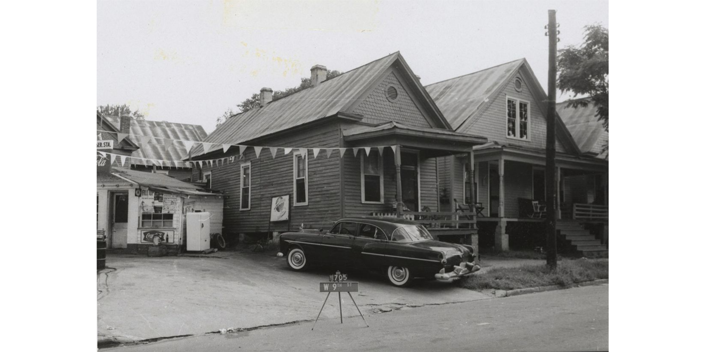 Two neighboring houses with a car parked beside the house on the left. Streamers are attached to the house on the left.