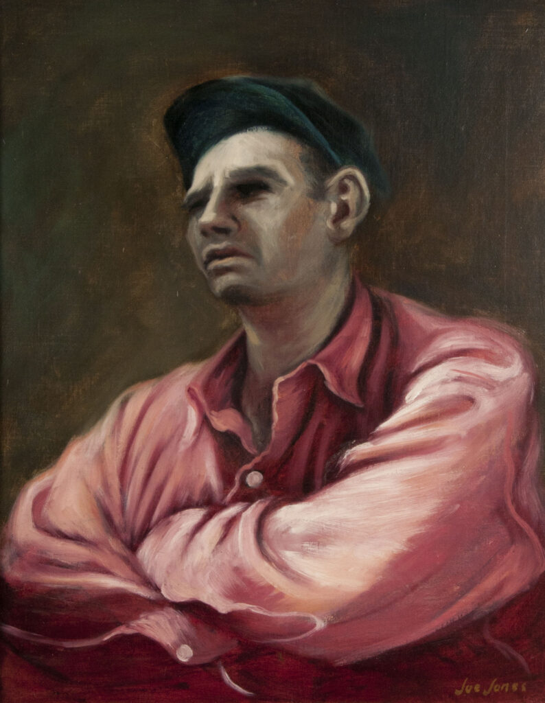 Portrait of a man in a red button down shirt and a hat, looking off in the distance with arms crossed in front of his chest.