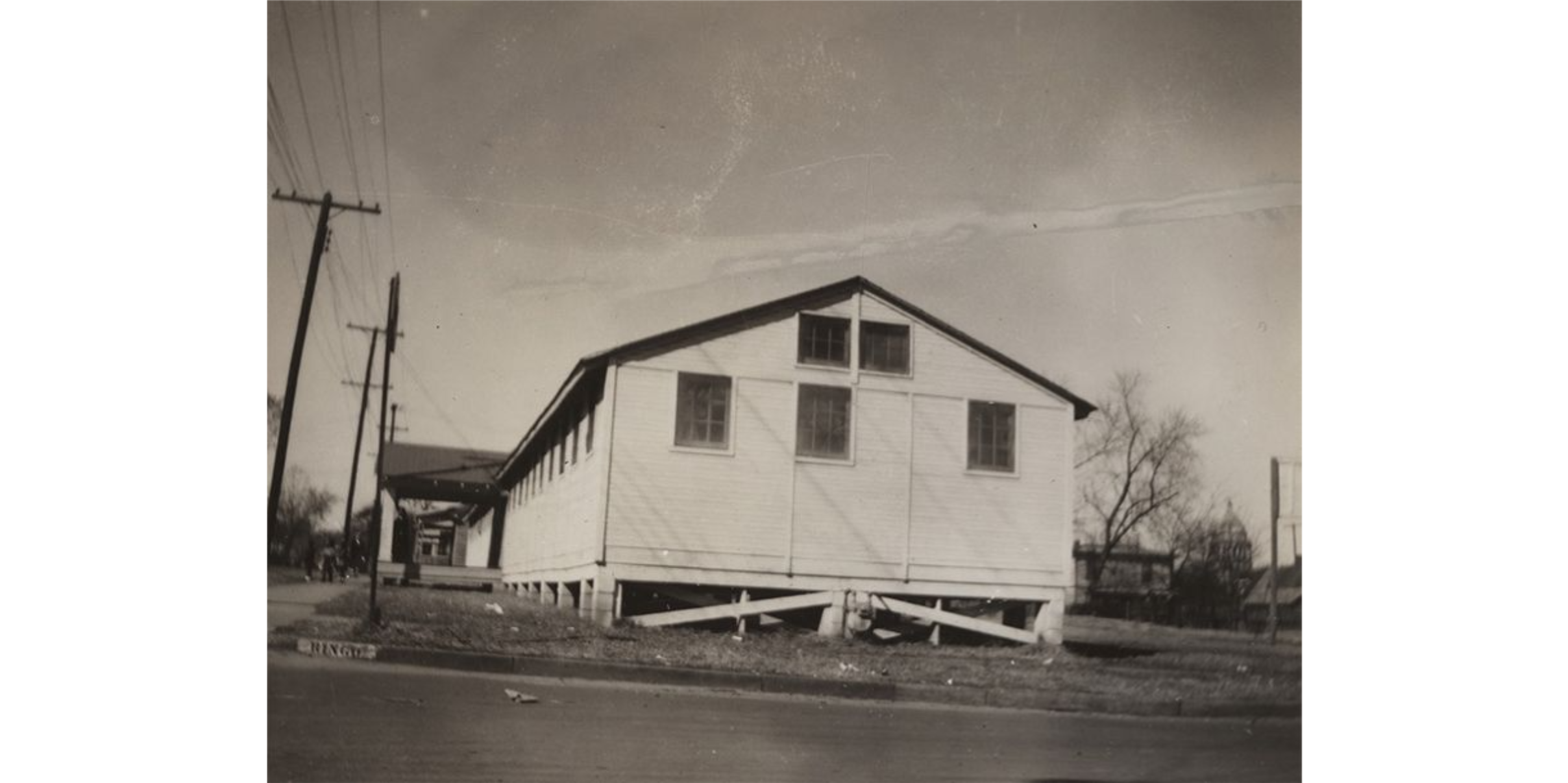 A sepia photograph of a frame building. A street marker on the left side of the photo reads: "Ringo."