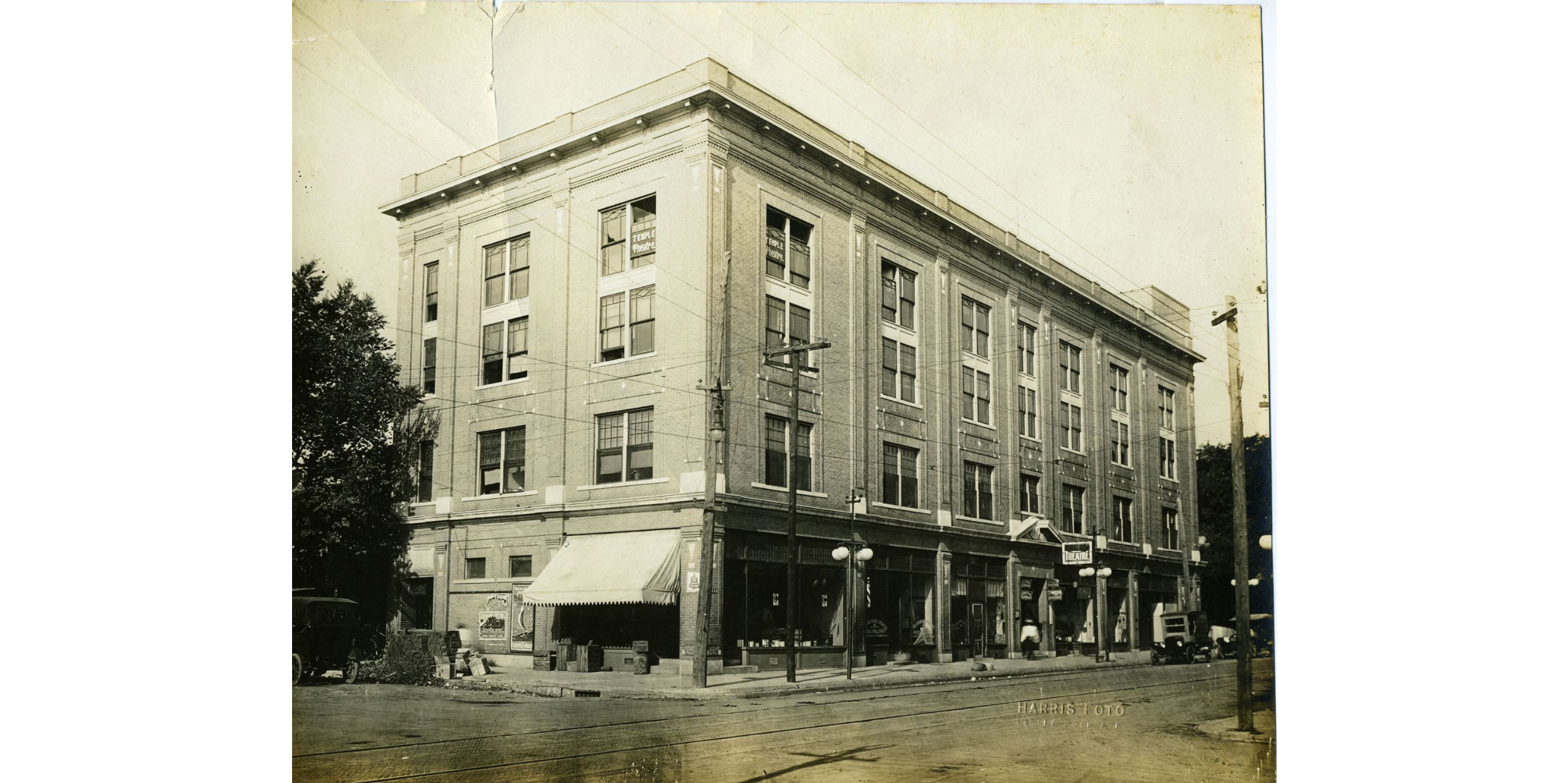 A multi-storied brick building on a corner lot. A sign in a window on the top floor reads: "Temple Theatre."