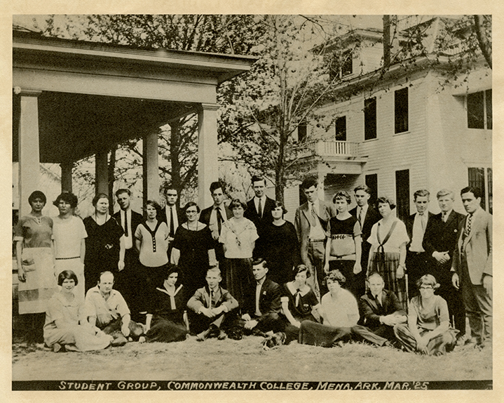 A group of people outside posing for a photo with two structures in the background. There are two rows of people standing, and a row of people sitting in the front.
