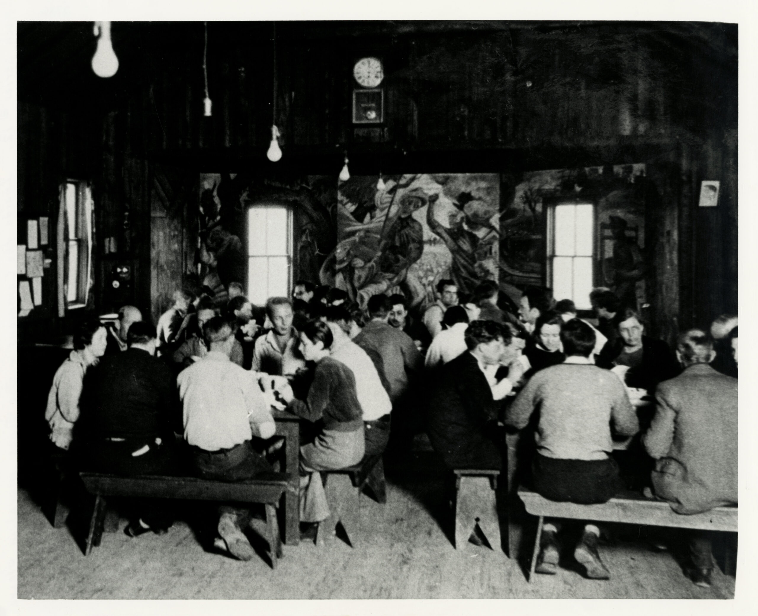 the interior of a room where people are seated at tables. A mural is on the back wall. 