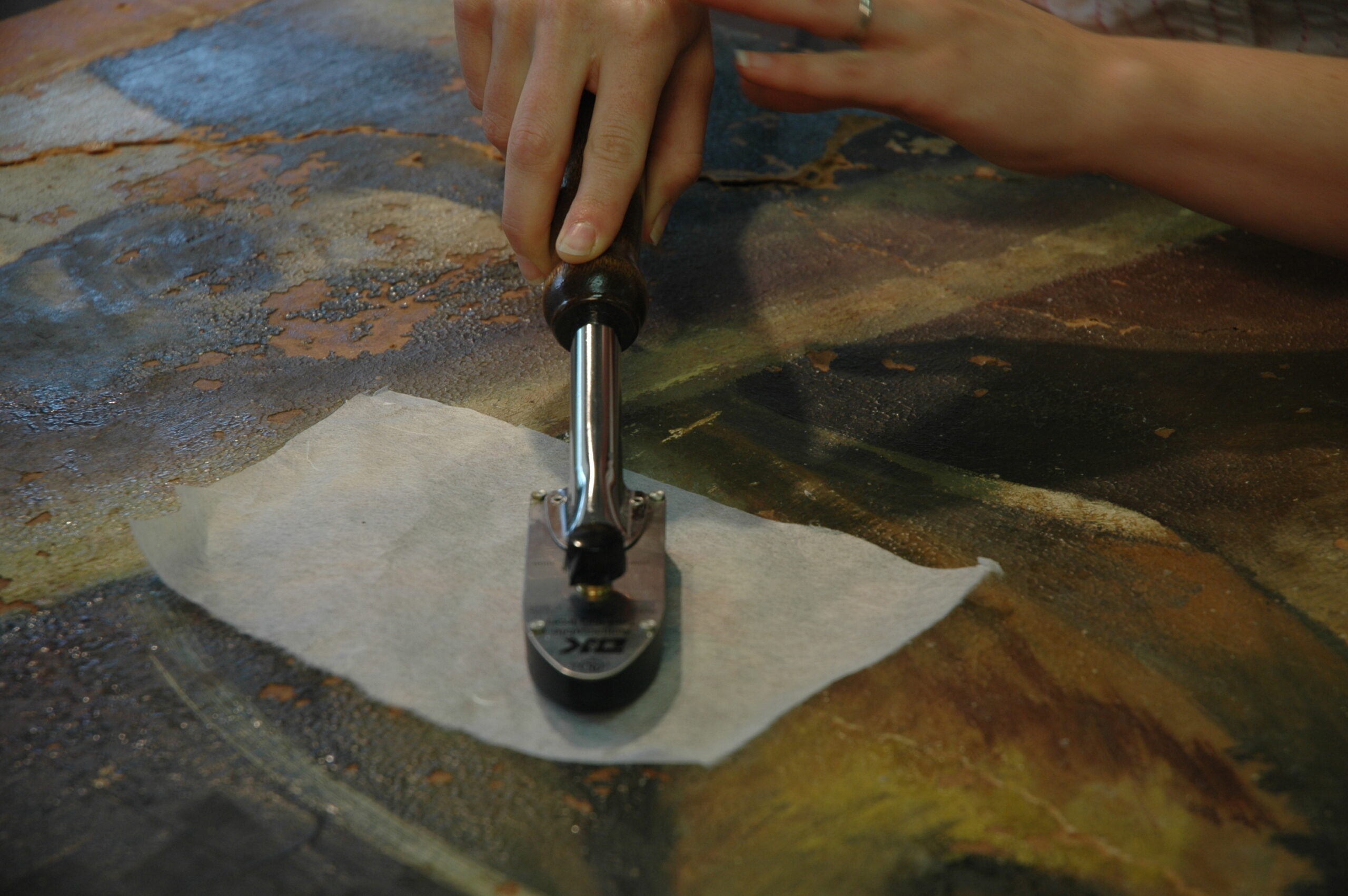 A close up of a tacking iron being used for conservation work on a painting.