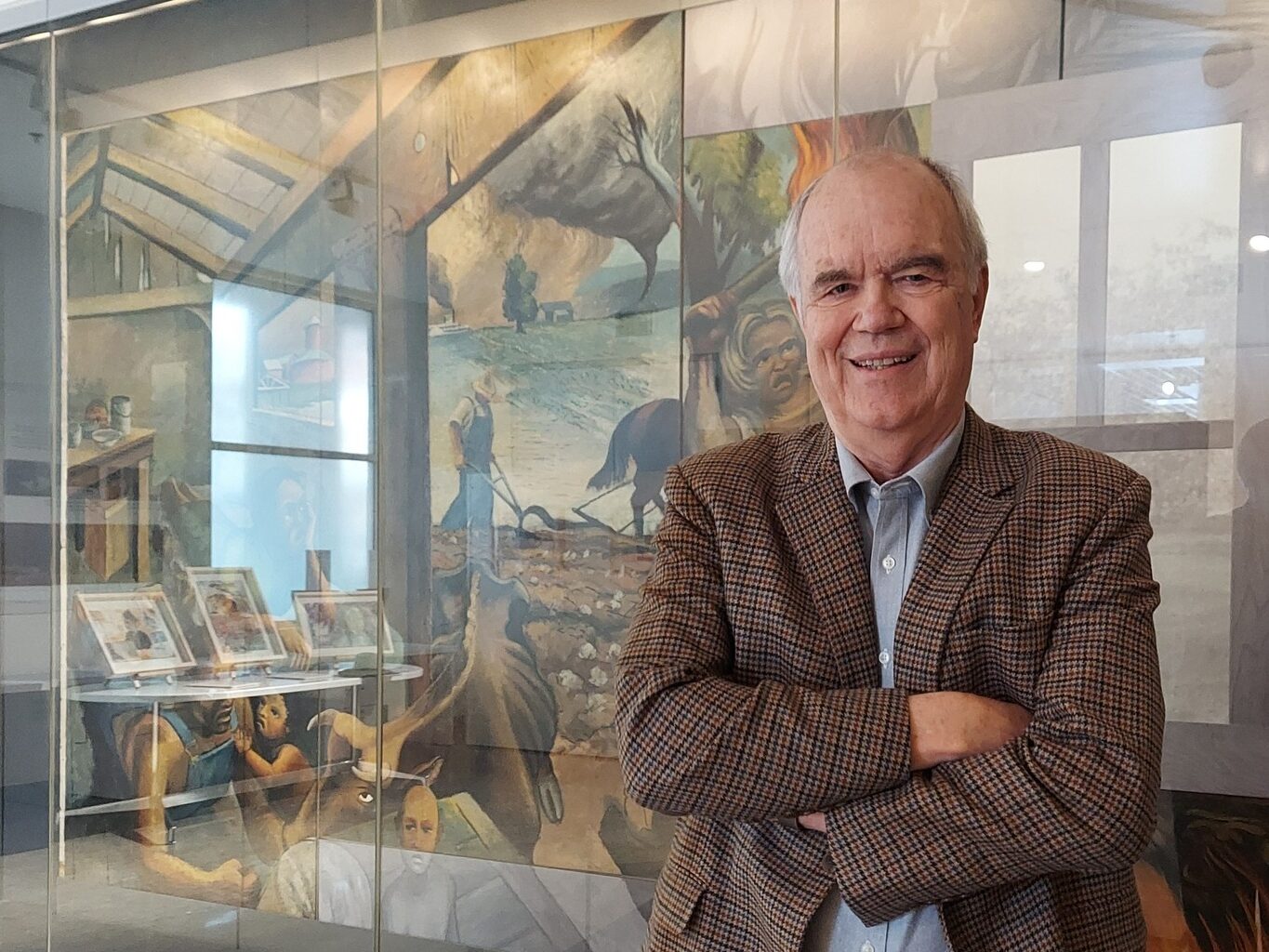 A man in a blazer posing with his arms crossed and standing in front of a mural.