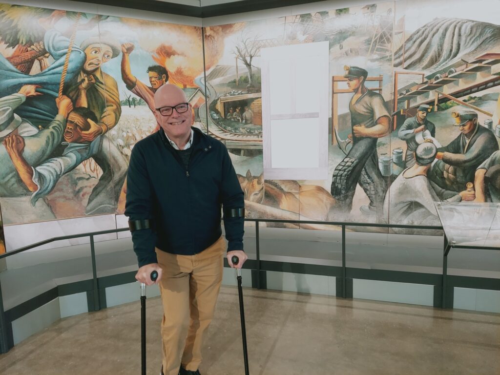 A man with glasses standing in front of a mural.