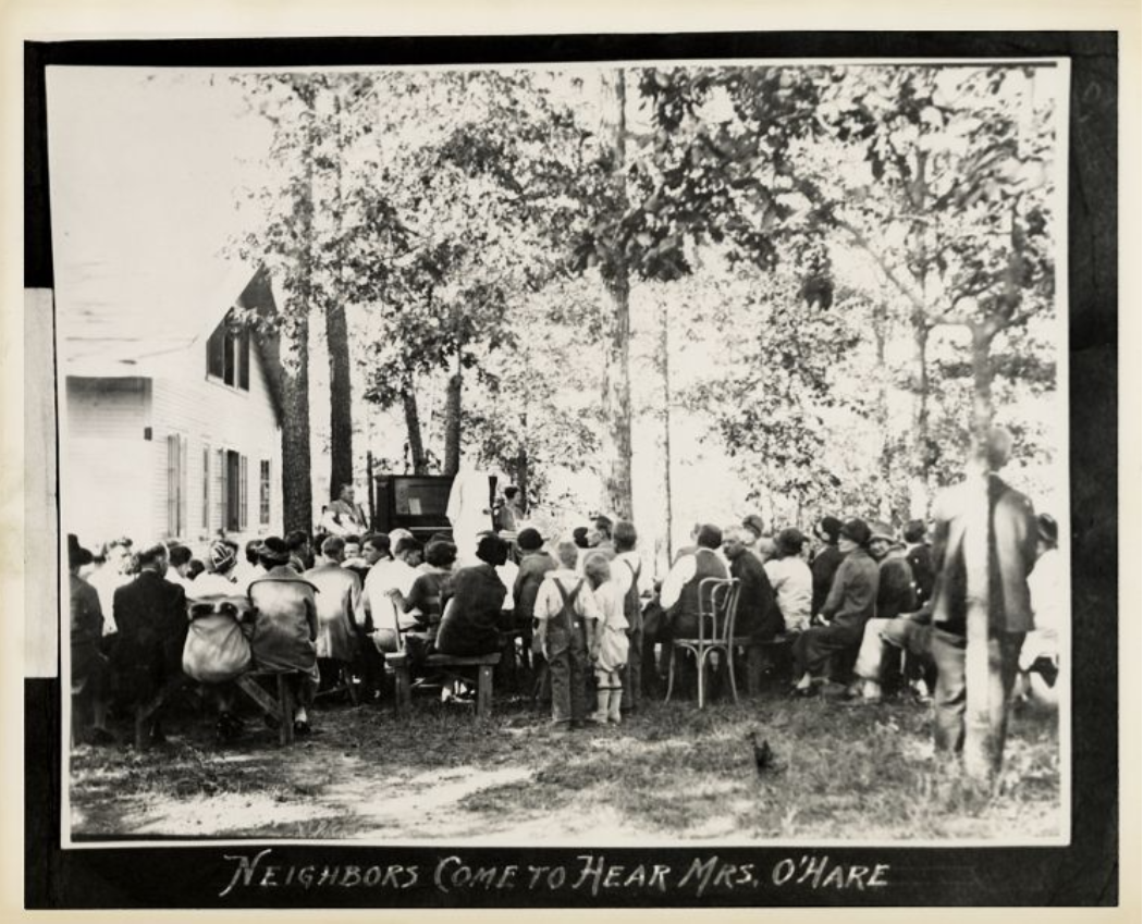 A crowd of people seated outside, listening to a speaker. The caption reads: "neighbors come to hear Mrs. O'Hare."