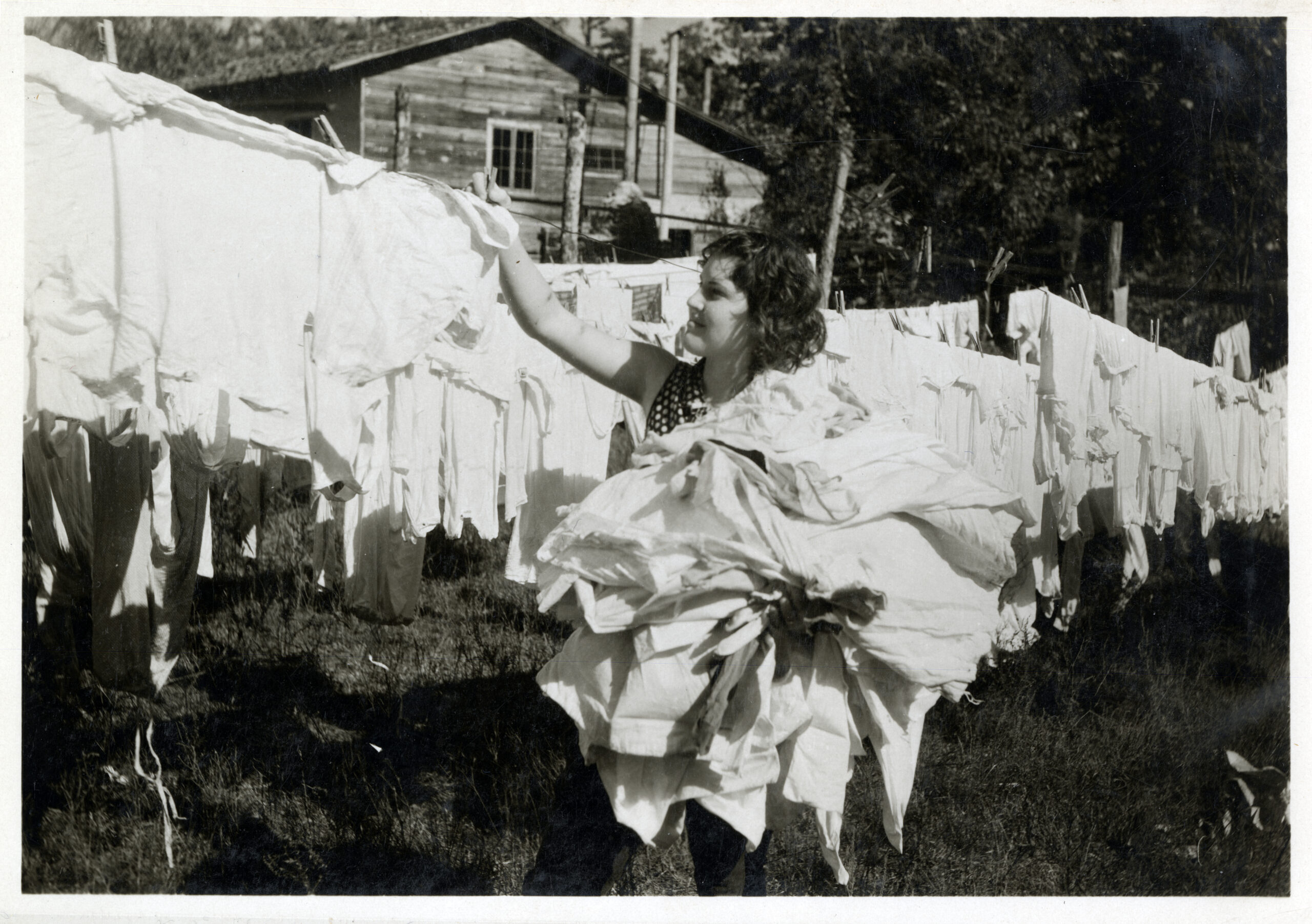 A woman with a pile of laundry in her arms standing at a clothesline.