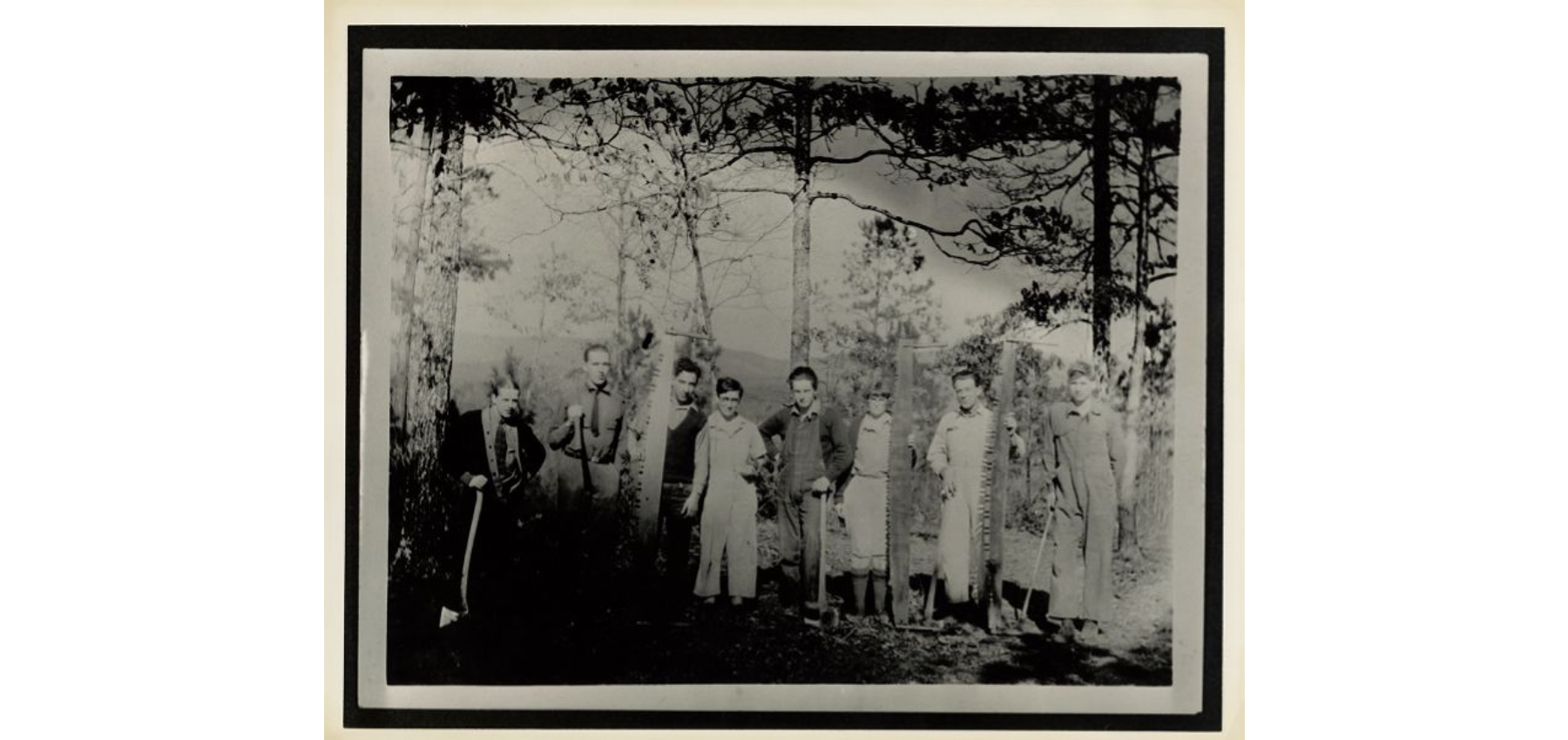 Eight people standing in a row. Three people are holding large lumber saws, while the others are holding axes.