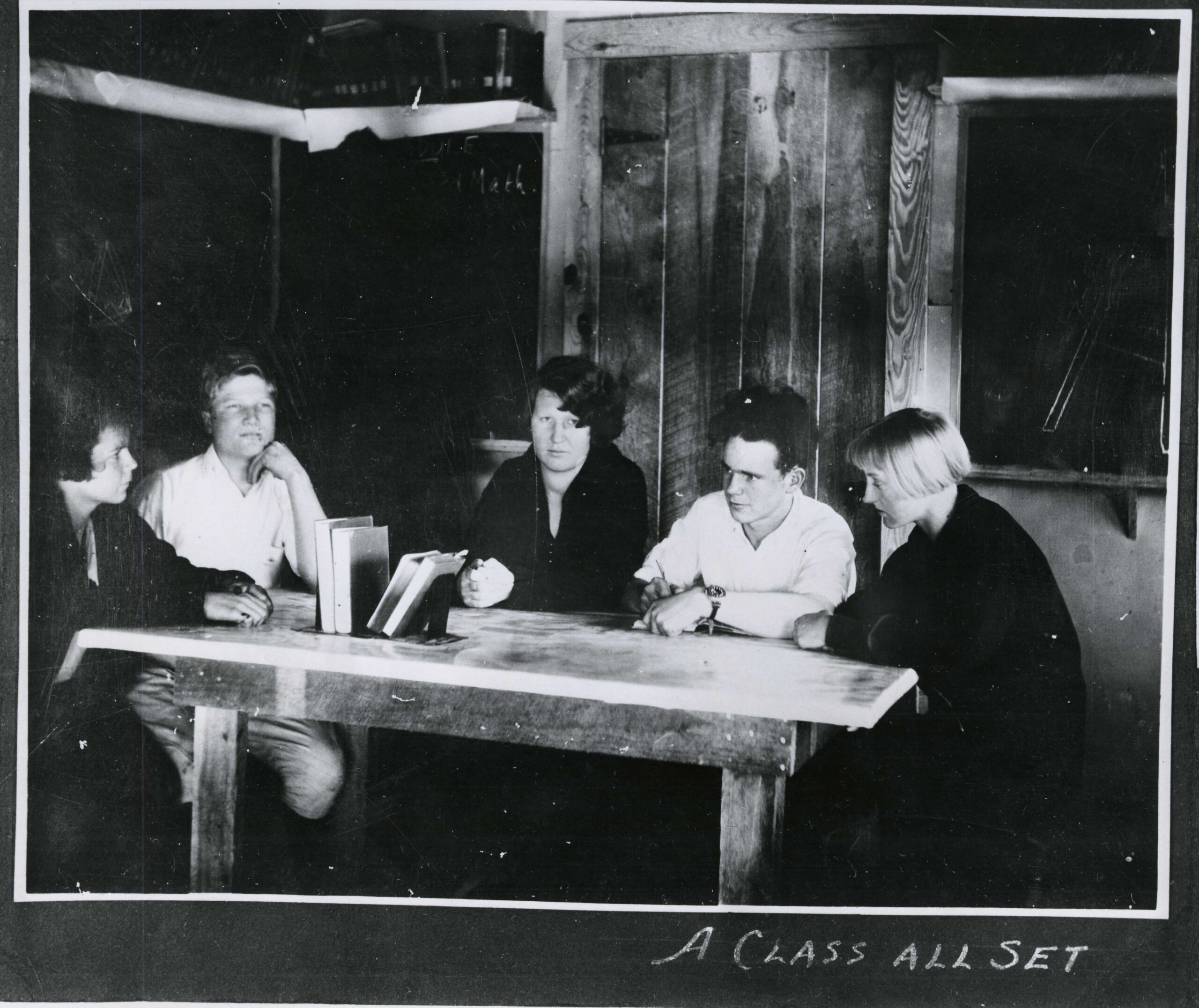 Five people sitting around a wooden table with books in the center.
